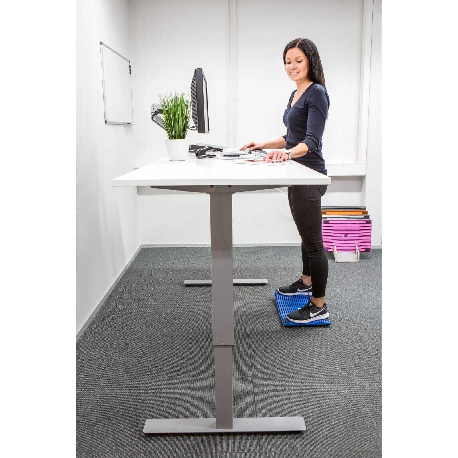 Woman using Gymbailu activation board at standing desk for improved movement and health in office setting.