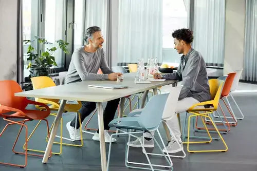 Two people seated on colorful Numo active chairs at a modern office table, showcasing ergonomic design and style.