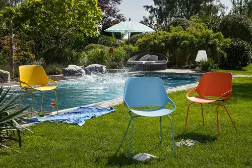 Colorful outdoor chairs by a poolside garden with lush greenery and umbrella in the background.