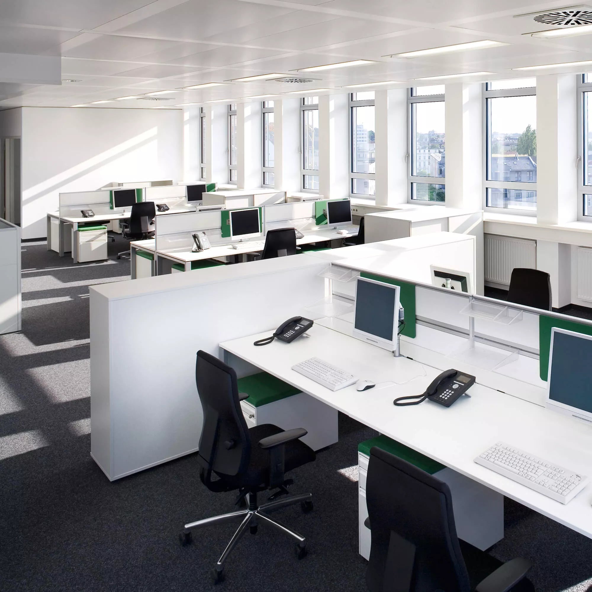 Modern office space featuring black ergonomic chairs and white desks with computers, phones, and green accents.